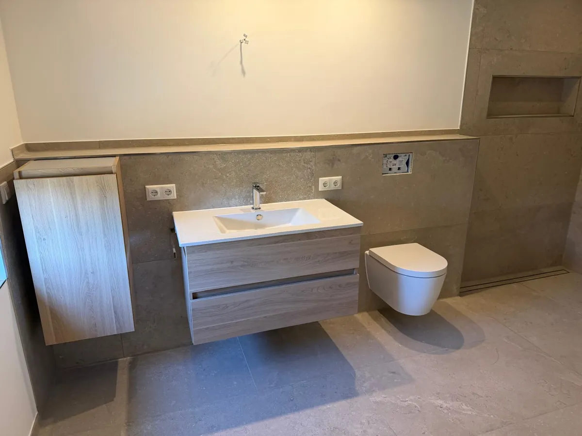 Waschtisch mit Unterschrank und Wand-WC vor großformatigen Fliesen in Steinoptik