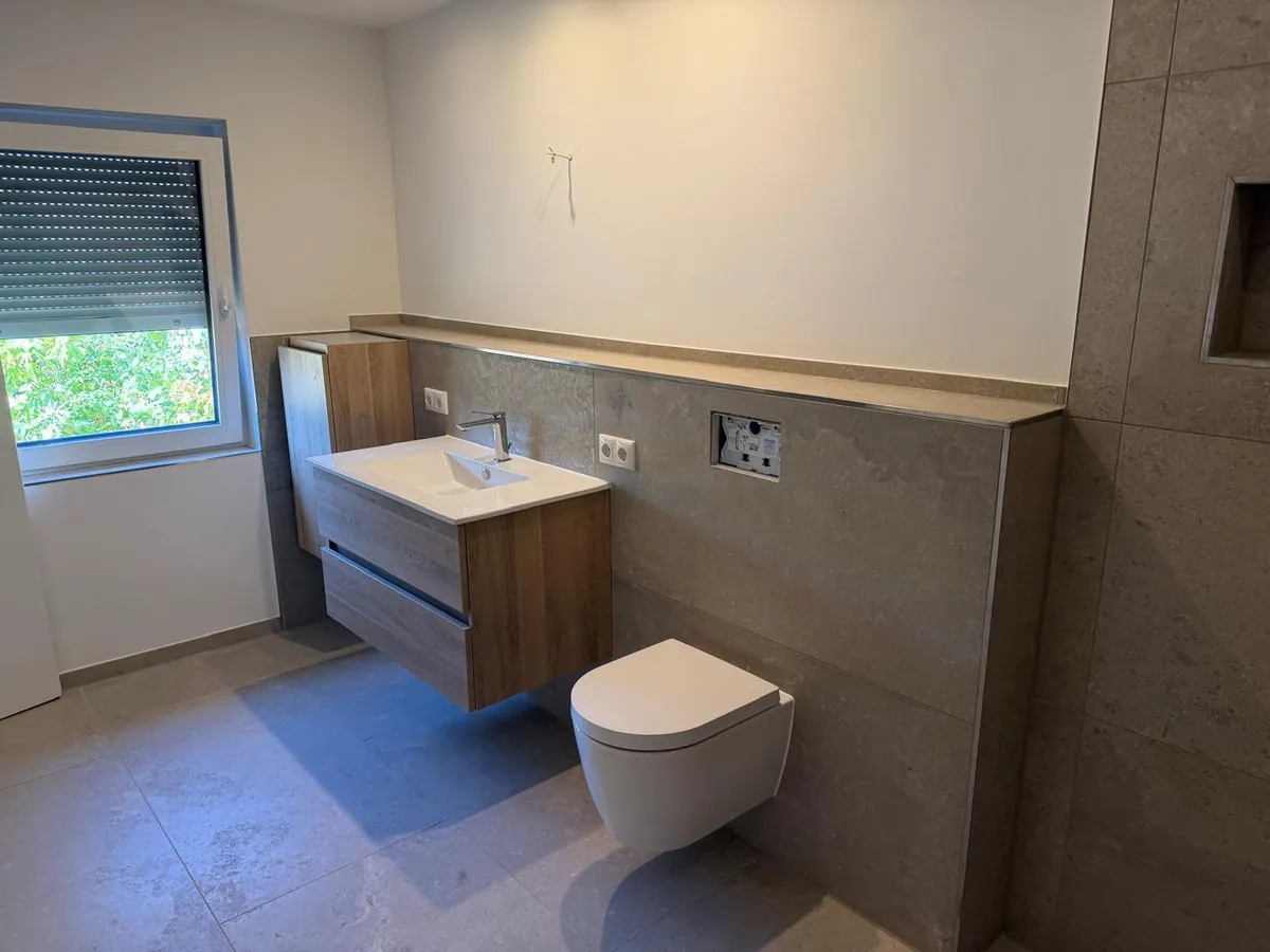 Neues Badezimmer mit Hängewaschtisch, Wand-WC und großformatigen Fliesen in Steinoptik