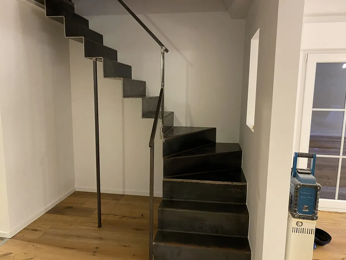 Innentreppe mit Holzdielenboden und schwarzem Metallgeländer